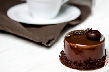 Bir ahşap stand yanında beyaz bir masada duran beyaz bir fincan lezzetli çikolatalı pasta çikolata parçaları ile yatıyor