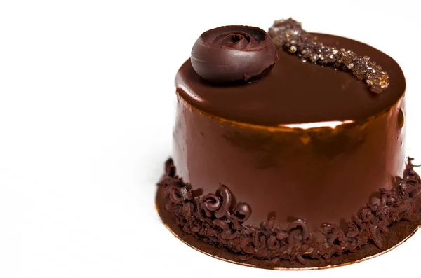 Un delicioso pastel de chocolate con trozos de chocolate se encuentra en un soporte de madera junto a una taza blanca, que se encuentra en una mesa blanca —  Fotos de Stock