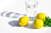 Citrony, čerstvé zelené máty a skleněné sklo s vodou na bílém podkladu. Stíny na bílém pozadí