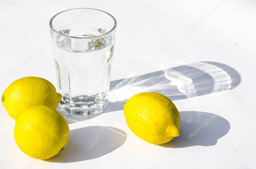 Lemons, fresh green mint and a glass glass with water on a white background. Shadows on a white background