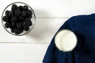 Siyah böğürtlen ve beyaz ahşap bir masa üzerinde bir bardak süt standı. Köy stili