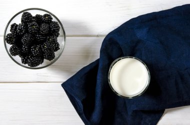 Siyah böğürtlen ve beyaz ahşap bir masa üzerinde bir bardak süt standı. Köy stili