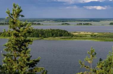 Ağaçların ve çimenlerin mavi gökyüzüne karşı yetiştiği adalar ile büyük bir nehir
