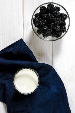 Siyah böğürtlen ve beyaz ahşap bir masa üzerinde bir bardak süt standı. Köy stili