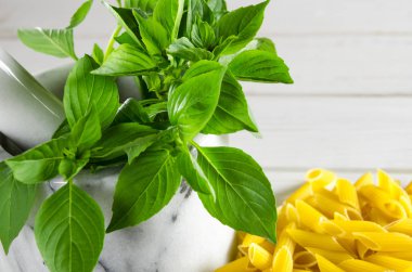 Mermer bir harç ve beyaz ahşap bir masa üzerinde yapıştırın yeşil fesleğen yaprakları