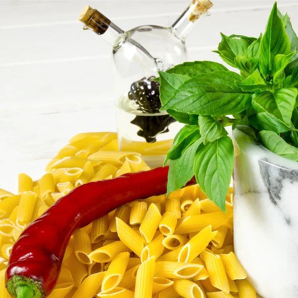 Pâtes, piment, basilic vert et huile d'olive sur une table en bois blanc — Photo