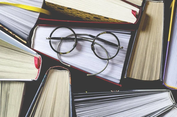 Sok tarka vastag nyitott könyv áll egy sötét háttér. A könyv a régi, kerek szemüveg és egy nyitott jegyzetfüzet ceruzával. — Stock Fotó