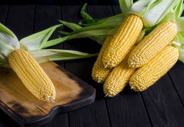 Siyah bir ağaç masada yeşil yaprakları ile sarı sulu mısır