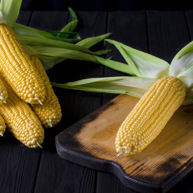 Siyah bir ağaç masada yeşil yaprakları ile sarı sulu mısır