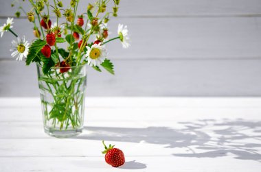 Şifalı otlar: kırmızı olgun çilek dalları, beyaz papatyalar ve nane yaprakları ahşap bir saç üzerinde bir bardak su standı