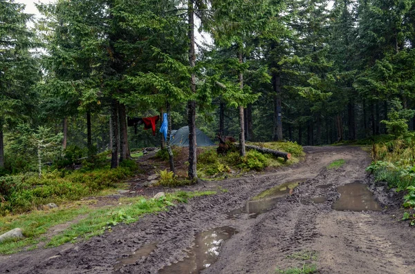 Bir fırtına dan sonra su birikintileri ile Kirli dağ yolu çadıra gitmek, hangi kuru ıslak ceketler yanında — Stok fotoğraf