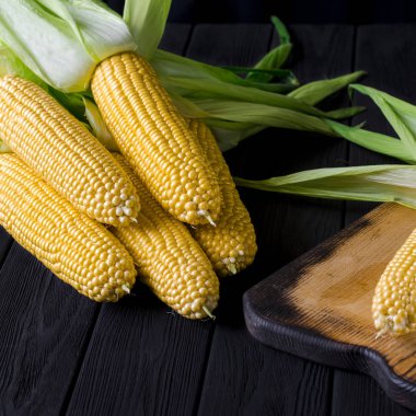 Siyah bir ağaç masada yeşil yaprakları ile sarı sulu mısır