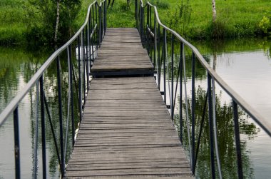 Metal korkuluklar ile dar bir ahşap köprü kıyıya nehir boyunca yol açar
