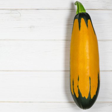 Yeşil kuyruklu renkli turuncu kabak beyaz ahşap bir masa üzerinde yatıyor