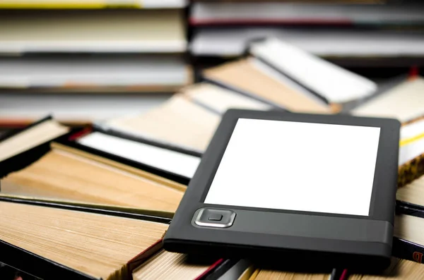 The e-book with a white screen lies on the open multi-colored books that lie on a dark background, close-up