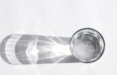 Beyaz arka planda güçlü gölgeleri olan su bardağı