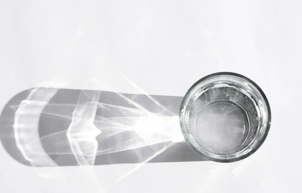 Beyaz arka planda güçlü gölgeleri olan su bardağı