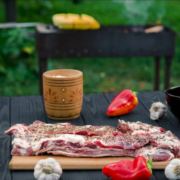 Bir salamura domuz kaburga biber, sarımsak, ızgara arka plan üzerinde mısır yanında bahçede ahşap bir masa üzerinde yalan — Stok fotoğraf