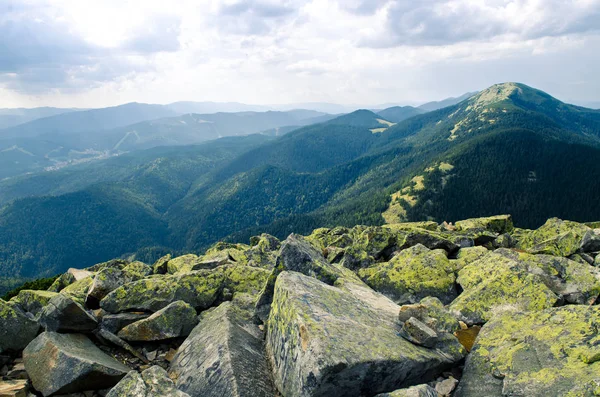 Enormes piedras cubiertas de líquenes verdes yacen en la cima de la montaña contra el telón de fondo de antiguas y altas cadenas montañosas. — Foto de Stock