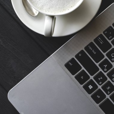 Dizüstü köpüklü bir fincan kahveyanında siyah ahşap bir masa üzerinde duruyor