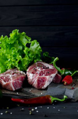 İki sulu biftek kırmızı ve yeşil biber ve siyah ahşap bir masada taze yeşil salata yanında vahşi bir taş üzerinde yalan