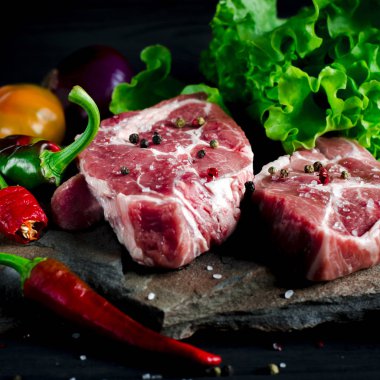 İki sulu biftek kırmızı ve yeşil biber ve siyah ahşap bir masada taze yeşil salata yanında vahşi bir taş üzerinde yalan