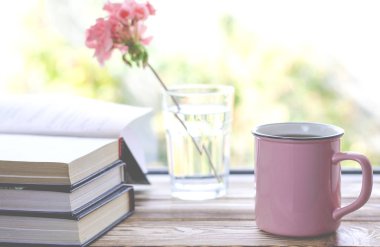 Kitap ve pembe sardunya çiçek duruyor bir bardak yanında ahşap bir pencere üzerinde çay ile pembe bir fincan duruyor