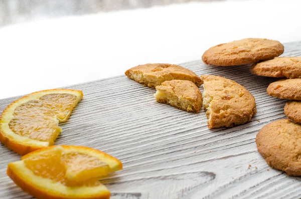 Круглые апельсиновые печенья с красочными засахаренными фруктами и ломтиком сочного апельсина, лежащего на деревянном столе на фоне зимнего леса — стоковое фото
