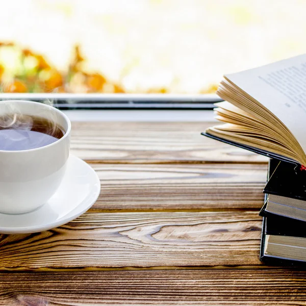 Una taza de té blanco se encuentra en un alféizar de madera junto a los libros en el fondo de la ventana — Foto de Stock