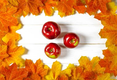 Sarı akçaağaç yaprakları ve kırmızı sulu elma beyaz ahşap arka plan üzerinde yalan