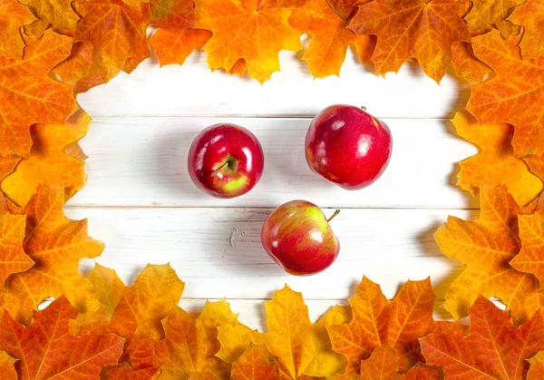 黄色のカエデの葉と赤いジューシーなリンゴは、白い木の背景に横たわっています — ストック写真