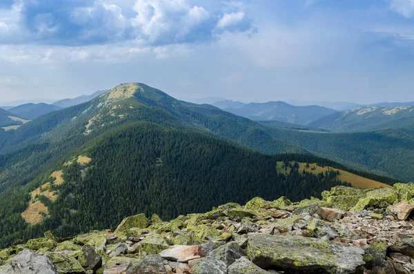 Yeşil likenlerle kaplı büyük taşlar, eski, yüksek sıradağların arka planında dağın tepesinde yatıyor.