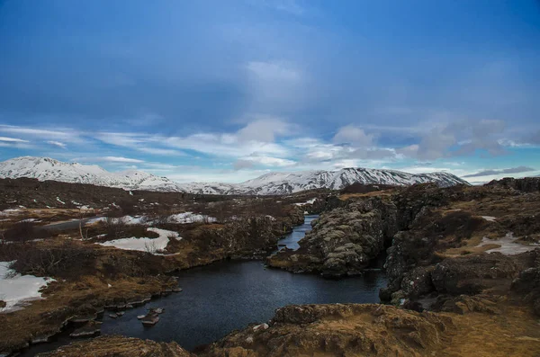 Typowy islandzki krajobraz: Park Narodowy Thingvellir, rzeki, pola lawy pokryte śniegiem na tle gór i nieba — Zdjęcie stockowe