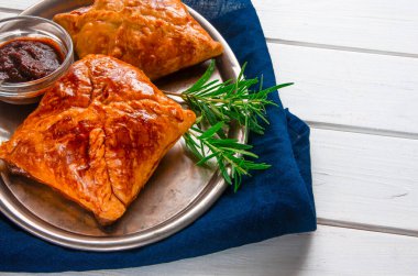 Ev yapımı hamur işleri et ve biberiyeli baharatlı sos mavi peçetedeki metal tepside servis edilir.