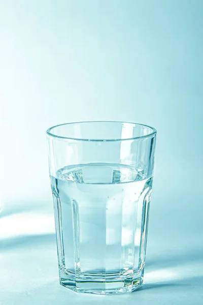 Glass with pure clear melt water on a blue background next to a couoshma with water