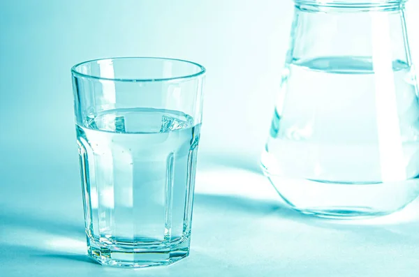 Glass with pure clear melt water on a blue background next to a couoshma with water