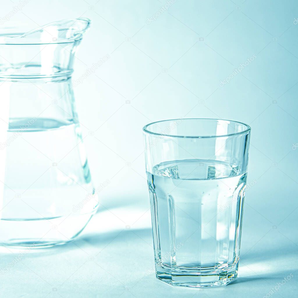 Glass with pure clear melt water on a blue background next to a couoshma with water