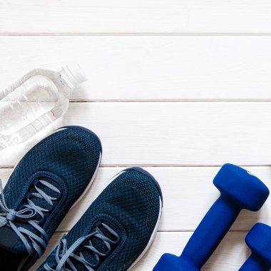 Spor çantası. Sağlıklı bir yaşam tarzı için spor malzemeleri. Mavi kadın ayakkabıları, mavi halterler ve beyaz pullar beyaz ahşap arka planda duruyor.