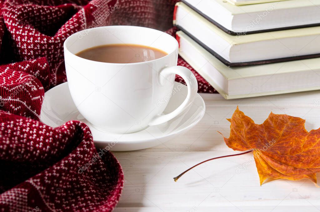 A cozy concept. A cup of coffee, a warm scarf and books stand on a white wooded background