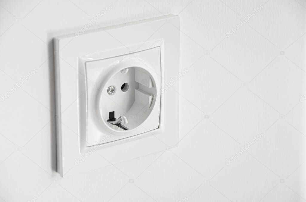 The white plastic socket is mounted in a white wall. Repair