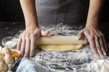 Hamur yoğuran eller, beyaz buğday unu serpiştiren hamurlar. Düşük tuş atışı, ellere yakın çekim, masada bazı malzemeler.