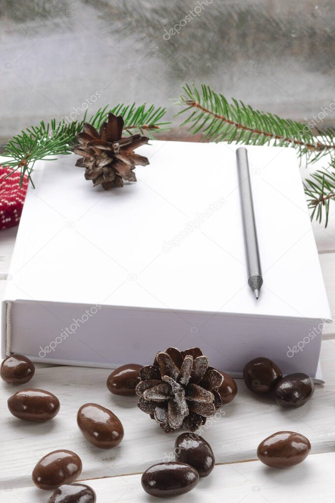 White book with black pencil lies on a white window sill next to chocolates