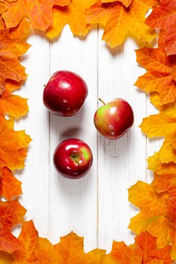 Elmaların sonbahar hasadı beyaz bir ahşap masada yatar. Sonbahar yaprakları