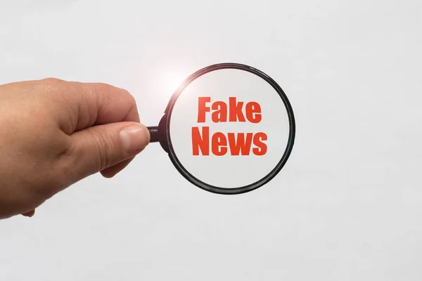 Lupa na mão e uma palavra Fake News no fundo branco — Fotografia de Stock