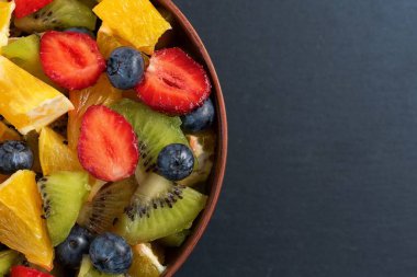 Tabak koyu arka plan üzerinde sağlıklı taze meyve salatası. Üstten görünüm