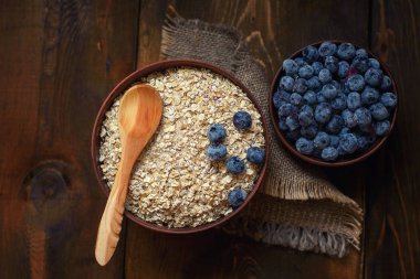 Koyu ahşap arka plan üzerinde sağlıklı bir kahvaltı: yulaf ezmesi, süt, yaban mersini. Üstten görünüm.