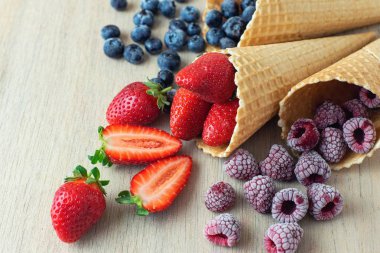 Çilek, yaban mersini, ahududulu waffle koniler hafif ahşap zemin üzerinde. Yakın çekim.