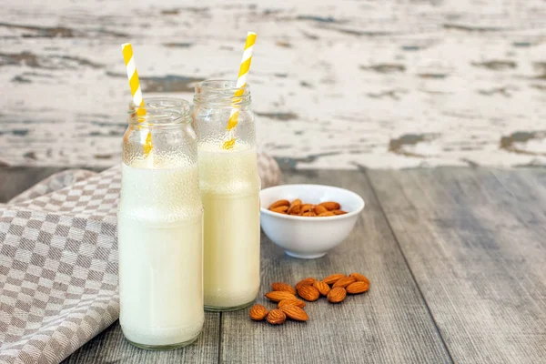 Almond milk in glass bottles and almonds on grey wooden background.