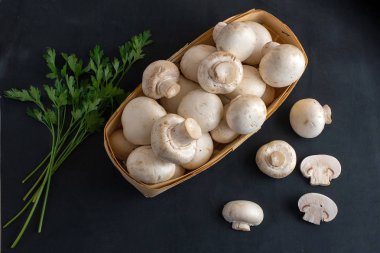 Karanlık bir arka plan üzerinde bir sepet içinde taze bütün ve dilimlenmiş champignon kümesi mantar. Üstten görünüm.