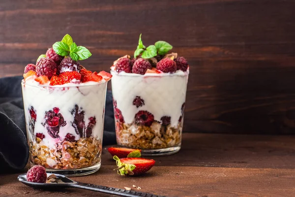 müsli ve meyveleri koyu ahşap masa üzerinde iki bardak yoğurt.